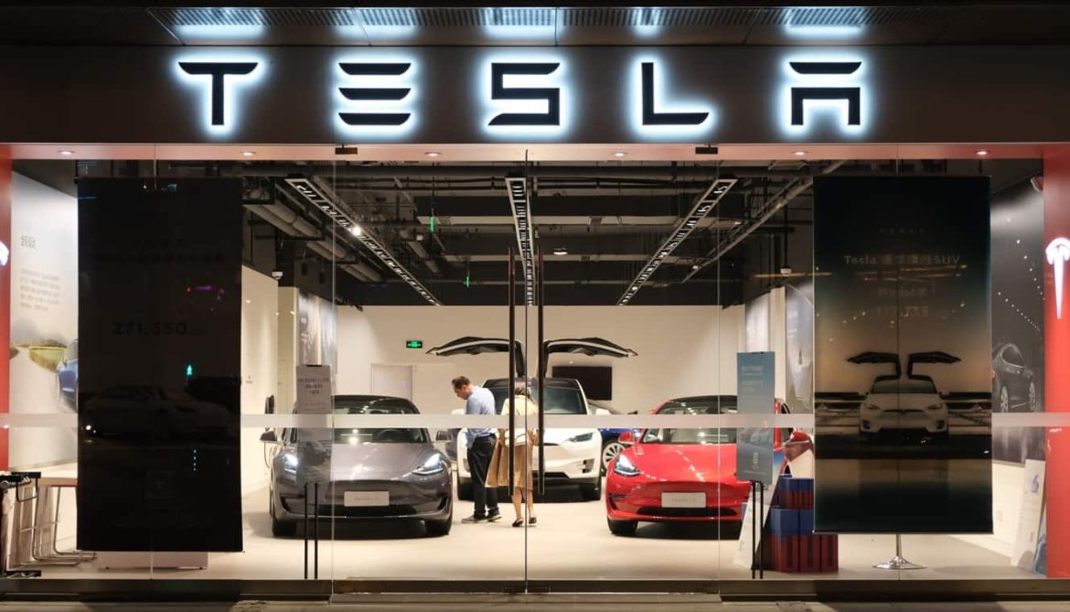 Façade vitrée d'une concession de voitures électriques Tesla illuminée la nuit avec plusieurs véhicules exposés dans le showroom.