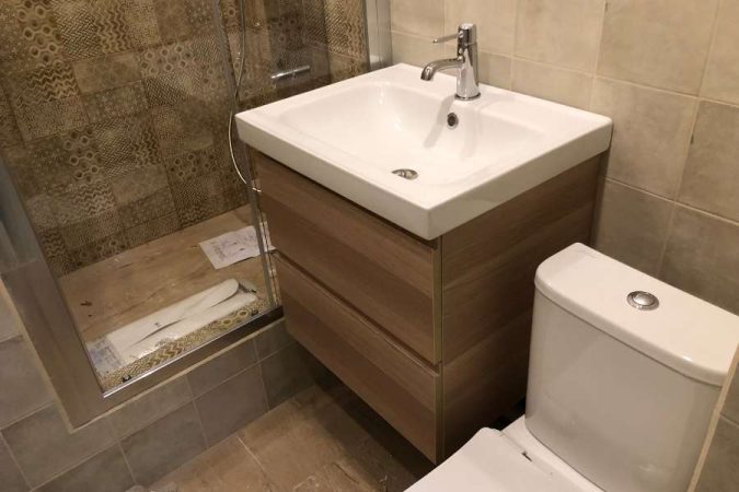 Un meuble vasque en bois clair avec un lavabo mural moderne intégré, placé dans une petite salle de bains près d'une douche.