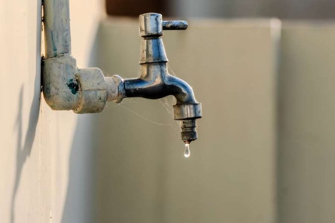 Un robinet qui goutte extérieur fixé sur un mur clair.